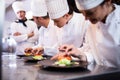 Head chef overlooking other chef preparing dish