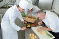 head-chef teaching colleagues how to slice vegetables in kitchen