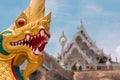 The head of a golden dragon against the background of the white Buddhist temple Wat Kaew Korawaram