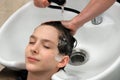 The head of the guy with his eyes closed lies over the sink, when a woman washes his head in the beauty salon. The female hands of Royalty Free Stock Photo