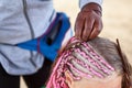 Head of little girl with woman mades thin plaits in African style, braiding process