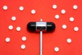 Head of reflex hammer is on red background surrounded by pills or tablets with ornament of polka dots. Concept photo diagnosis, tr