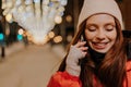 Head shot of cheerful young woman in hat and winter jacket talking using smartphone standing on snow city street on Royalty Free Stock Photo