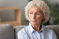 Head shot older woman lost in thoughts, sitting on couch