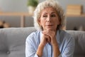 Head shot peaceful older woman dreaming alone, sitting on couch