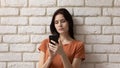 Head shot serious young woman using phone, brick wall background Royalty Free Stock Photo