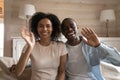 Happy african american family couple waving, sitting on sofa. Royalty Free Stock Photo