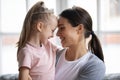 Happy little blonde girl touching foreheads with young mother.