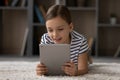 Head shot little girl using tablet, lying on warm floor