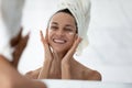 Head shot mirror reflection smiling woman applying moisturizing face cream