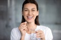 Cheerful woman holding pill glass of water looking at camera