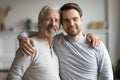 Elderly mature dad cuddling shoulders of grownup son.