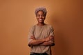 Smiling millennial African woman standing with folded arms over beige background Royalty Free Stock Photo