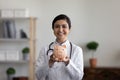 Head shot portrait smiling Indian female doctor holding piggy bank Royalty Free Stock Photo