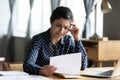 Stressed unhappy millennial indian girl looking through paper document.