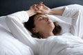 Stressed young brunette woman lying in bed with hands on head