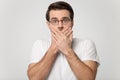 Head shot studio portrait millennial fearful man covering mouth.