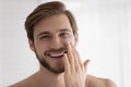 Head shot of young attractive guy applying moisturizer