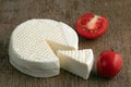 Head and slice of feta cheese on a wooden background with tomatoes.