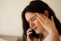 Headache. Close-up of exhausted overstressed girl and talking on the phone. Portrait of attractive young woman feeling