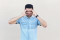 Headache, confusion or problem. Portrait of sick handsome young bearded man in blue shirt standing and holding his head and Royalty Free Stock Photo