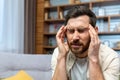 Headache of mature single man sitting on sofa alone at home and holding head with hands in living room Royalty Free Stock Photo