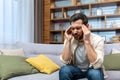 Headache of mature single man sitting on sofa alone at home and holding head with hands in living room Royalty Free Stock Photo