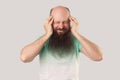 Headache, thinking or confusion. Portrait of middle aged bald man with long beard in light green t-shirt standing and holding his Royalty Free Stock Photo