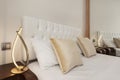 Headboard in a modern bedroom with white capitone upholstered headboard, gold cushions and twin decorative lamps placed next to a