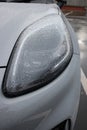 Headlamp on a grey car up close, taken on a rainy day, water droplets on headlamp and car