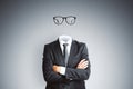 Headless invisible businessman in suit with folded arms and abstract glasses standing on gray wall background. Business and secret Royalty Free Stock Photo