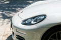 Headlight and front part of the hood of the white Porsche Panamera car parked on the street.