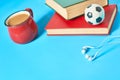 .Headphone, old books, toy basketball ball and red cup full of coffee on blue background Royalty Free Stock Photo