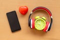 Headphones and alarm clock and smartphone and red heart on wooden desk. Musical concept