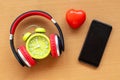 Headphones and alarm clock and smartphone and red heart on wooden desk. Musical concept