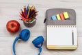 Headphones, apple, metal stand with color pencils and open exercise book on bag-pencil case with color felt pens and marker