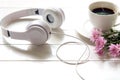 Headphones and coffee cup on wooden desk table with pink flower. Music and lifestyle concept.