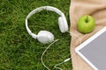 Headphones, electronic tablet and green apple for picnic in park