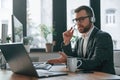 In headphones. Having online conversation. Businessman in suit is in the office with computer