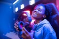 Headphones with microphone in hands of young african happy woman professional gamer online video game, neon background