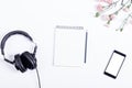Headphones, smart phone, paper notebook, pencil and flowers lie