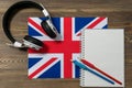 Headphones, a spiral notebook and two black-graphite pencils are lying on the flag of Great Britain. The concept of English