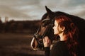 2 heads one love! stallion with head collar and redhead woman are bonding while being intimate friends and look left into sun to Royalty Free Stock Photo