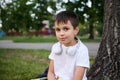Headshot of an adorable handsome cute boy, elementary school child sitting on the green grass of the park, resting during
