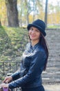 Headshot of adult girl with long straight dark brown hair in black bowler hat and leather jacket