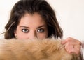 Headshot attractive brunette facing camera covering half her face with brown fur clothing, white studio background