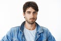 Headshot of attractive young hispanic man with blue eyes and beard in denim jacket over striped t-shirt looking at Royalty Free Stock Photo