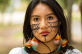 Headshot beautiful Amazonian woman, indigenous facial paint and earrings with colorful feathers, posing seriously for