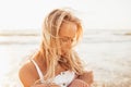 Headshot of beautiful blonde slim girlwearing white dress and cardigan on beach of sea or ocean against the sun. Youth Royalty Free Stock Photo