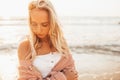 Headshot of beautiful blonde slim girlwearing white dress and cardigan on beach of sea or ocean against the sun. Youth Royalty Free Stock Photo